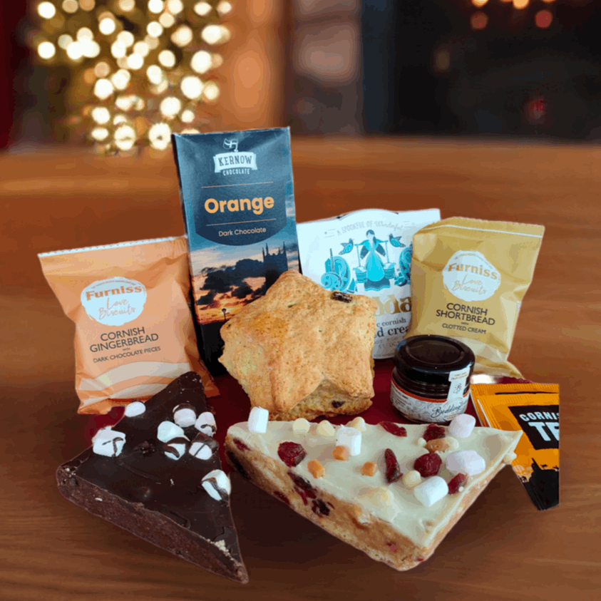 Assorted snacks and treats on a wooden surface with a festive background featuring lights and a fireplace.