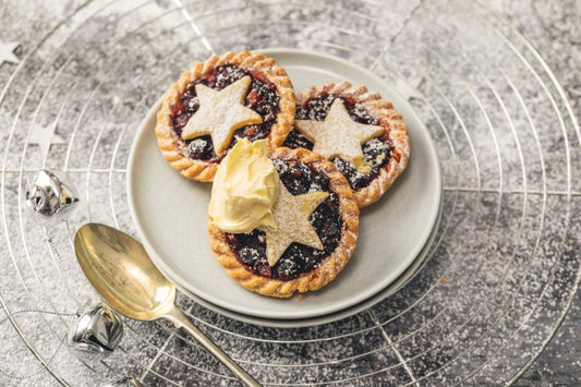 Three mince pies on a plate with a scoop of clotted cream, served on a textured surface.